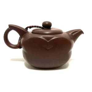 May include: A brown ceramic teapot with a rounded body, a curved handle, and a spout. The lid has a small knob and is attached to the handle with a brown cord. The teapot has a decorative design on the front.