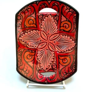 May include: A rectangular ceramic tray with rounded corners and two integrated handle cutouts. The surface features a vibrant red and orange glaze with a raised, embossed floral cross pattern in the center and black decorative line work.