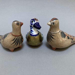 May include: Three ceramic bird figurines, two brown with black and red painted details, and one blue and white with a gold base.