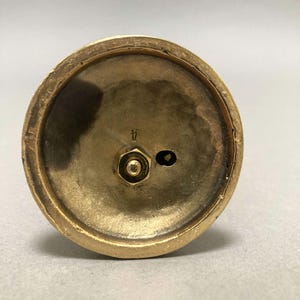 Op de afbeelding: De onderkant van een gouden metalen kandelaar met een schroef en de letter "H" gegraveerd op de basis.