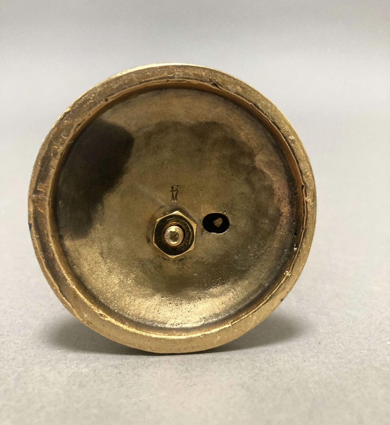 Op de afbeelding: De onderkant van een gouden metalen kandelaar met een schroef en de letter "H" gegraveerd op de basis.