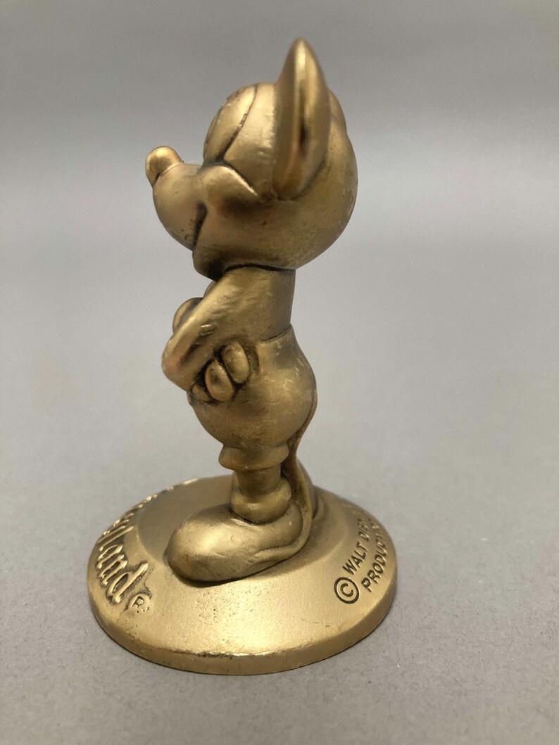 Op de afbeelding: Een gouden beeldje van Mickey Mouse dat op een ronde basis staat. De basis heeft de tekst "Walt Disney Productions" erop.