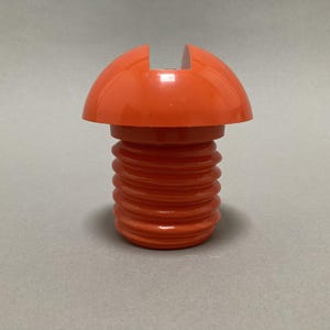 May include: An orange bottle stopper with a ribbed base and a rounded top with a vertical slit. The stopper is made of a glossy plastic material and is designed to fit into a bottle opening.