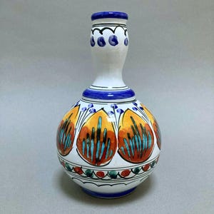 May include: A decorative ceramic vase with a bulbous body and a slender neck. The vase features a white base with orange, red, and turquoise floral patterns. The neck and base are accented with blue and black details. A unique piece for home decor.