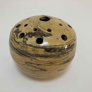 May include: A ceramic, spherical incense holder with a speckled tan and dark brown marbled design. The incense holder has multiple holes on the top and sides for releasing the fragrance. The overall shape is round and smooth.