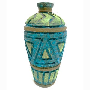 May include: A decorative vase with a textured surface. The vase features a color palette of teal, gold, and brown. Geometric patterns and horizontal bands adorn the vase's exterior. The vase has a narrow neck and a rounded body.