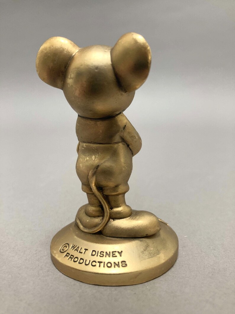 Op de afbeelding: Een gouden beeldje van Mickey Mouse dat op een voet staat met de tekst "&copy; WALT DISNEY PRODUCTIONS".