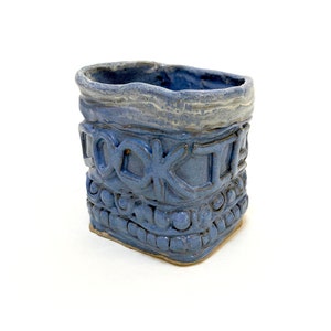 May include: A blue ceramic cookie jar with the word "Cookies" embossed on the front. The jar has a textured surface and a white glaze.