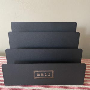 Mail holder, small black tin desk top style with sections.  Compact but will hold a week’s worth of envelopes.  Hand stamped MAIL in gold.