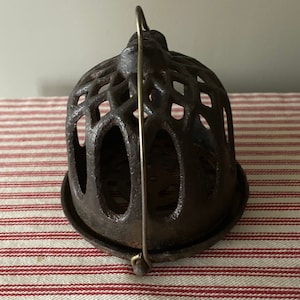 Pode incluir: Uma gaiola de ferro fundido com uma alça de arame. A gaiola é projetada para segurar uma vela ou outro objeto pequeno. Tem um design decorativo e intrincado.