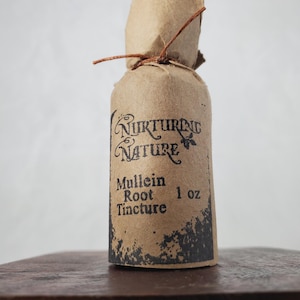 Puede incluir: Una botella de vidrio marrón con una etiqueta de papel marrón que dice "Nurturing Nature" y "Mullein Root Tincture 1 oz". La botella está atada con una cuerda.