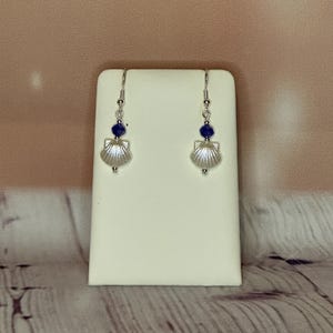 May include: A pair of silver earrings featuring a blue gemstone and a seashell design.