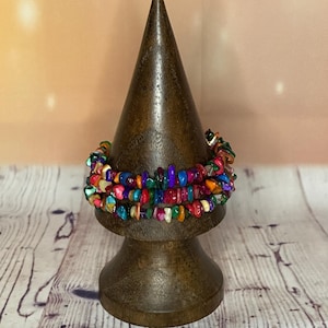 May include: Multicoloured beaded bracelet made of small, irregular shaped stones. The bracelet is stacked on a wooden display stand.