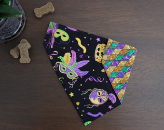 May include: A black bandana with a Mardi Gras theme. It features purple, green, and gold glitter, masks, feathers, and beads. The bandana is folded in half and has a purple, green, and gold glitter pattern on the back.