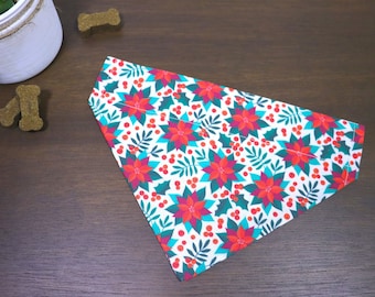 Puede incluir: Un pañuelo para perro blanco con un patrón de poinsettia y acebo rojo y verde.