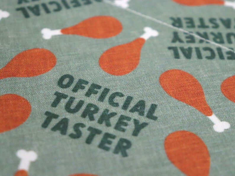 May include: Green fabric with the text "OFFICIAL TURKEY TASTER" in dark green letters. The fabric is decorated with a repeating pattern of orange turkey legs.