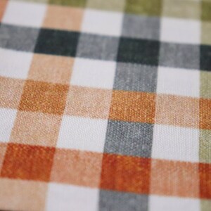 May include: A close-up of a white fabric with a checkered pattern in shades of orange, brown, green, and gray.