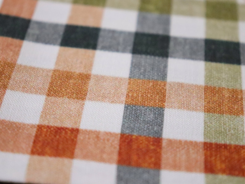 May include: A close-up of a white fabric with a checkered pattern in shades of orange, brown, green, and gray.