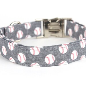 May include: A gray dog collar with a white baseball pattern. The collar has a silver buckle and D-ring.
