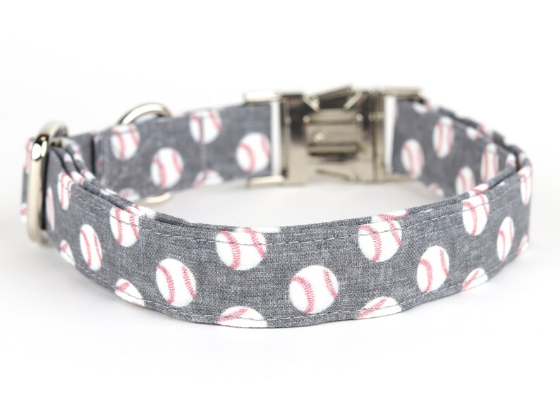 May include: A gray dog collar with a white baseball pattern. The collar has a silver buckle and D-ring.