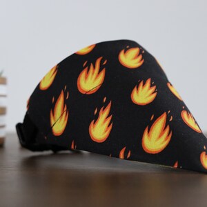 May include: Black bandana with a repeating pattern of yellow and orange flames. The bandana has a black adjustable strap.