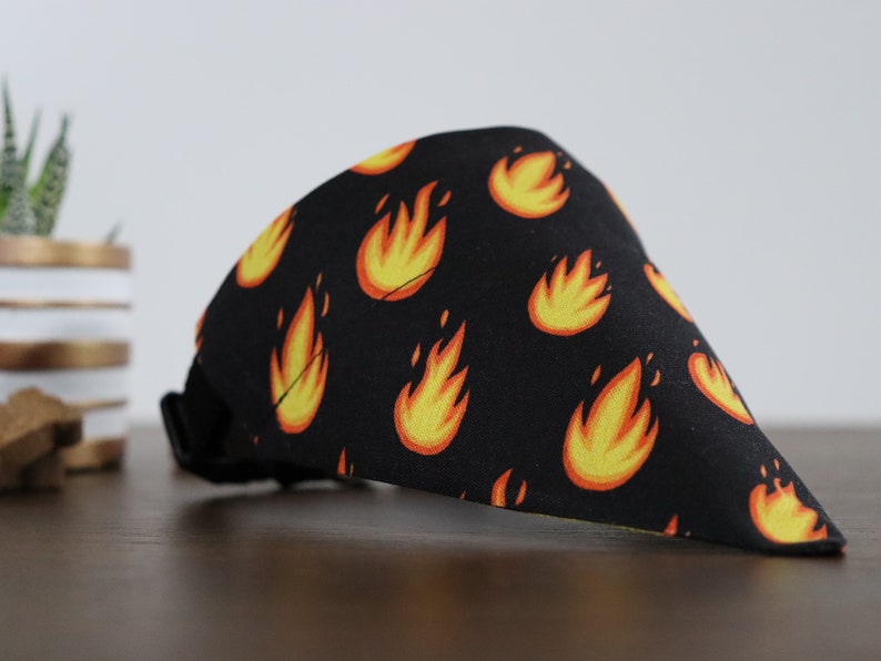 May include: Black bandana with a repeating pattern of yellow and orange flames. The bandana has a black adjustable strap.
