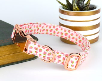 May include: A pink and white dog collar with a rose gold buckle and D-ring. The collar has a strawberry print.