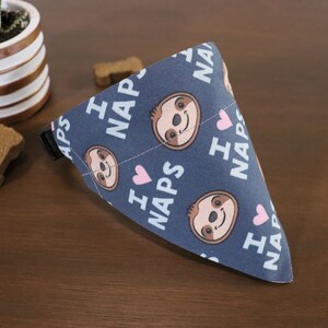 Puede incluir: Un pa&ntilde;uelo para perros azul marino con un patr&oacute;n repetido de perezosos de dibujos animados, corazones rosas y las palabras "I LOVE NAPS" en blanco. El pa&ntilde;uelo es triangular y tiene una hebilla negra.