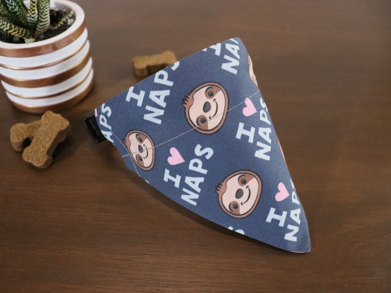Puede incluir: Un pa&ntilde;uelo para perros azul marino con un patr&oacute;n repetido de perezosos de dibujos animados, corazones rosas y las palabras "I LOVE NAPS" en blanco. El pa&ntilde;uelo es triangular y tiene una hebilla negra.