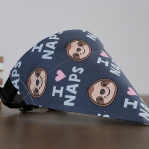 Puede incluir: Bandana azul marino para perros con un patr&oacute;n repetido de caras de perezosos sonrientes, corazones rosas y las palabras "I NAPS" en blanco. La bandana tiene un collar negro ajustable.