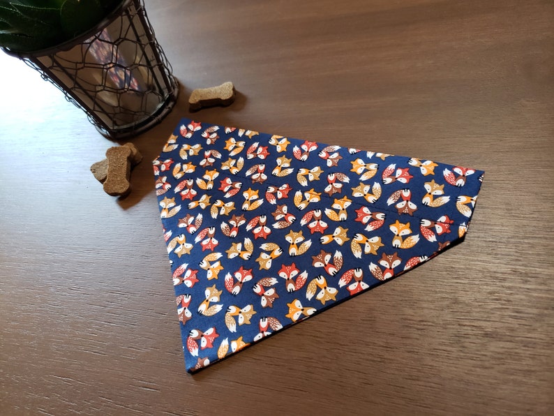 May include: A blue dog bandana with a pattern of orange, brown, and yellow foxes.