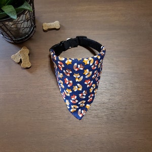 May include: A blue dog bandana with a pattern of orange and yellow foxes. The bandana is tied around a black collar.