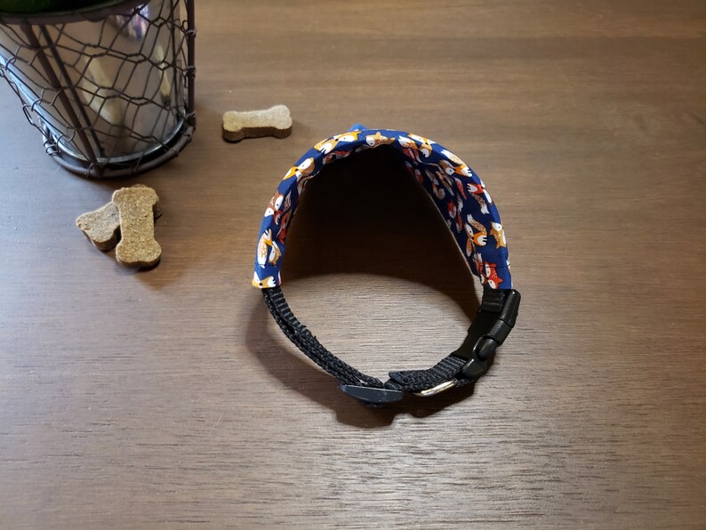 May include: A blue dog collar with a pattern of orange and white foxes. The collar has a black buckle.