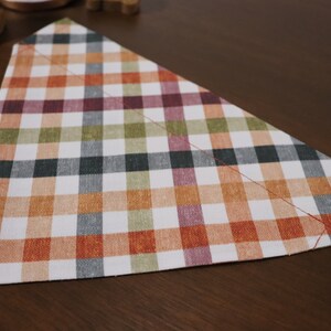 May include: A triangular dog bandana with a plaid pattern in shades of orange, green, black, and pink.