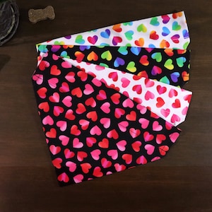 May include: Four dog bandanas with a heart pattern. The bandanas are in different colors, including black, white, and rainbow.