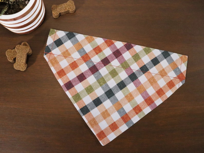 May include: A white, orange, green, and black plaid dog bandana with red stitching.
