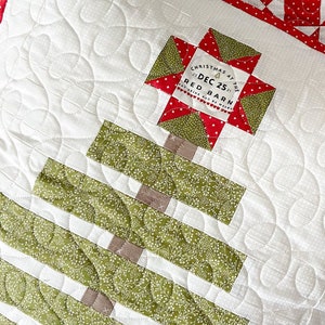 May include: A white quilted pillow with a green and brown Christmas tree design. The pillow has a red and white star-shaped fabric label with the text "Christmas at the Red Barn Dec 25"