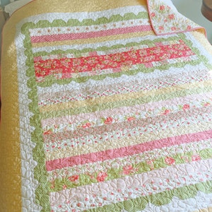 Peut inclure: Une courtepointe en patchwork avec un motif floral dans des tons de rose, vert et jaune. La courtepointe est matelassée avec un bord festonné et un motif floral.