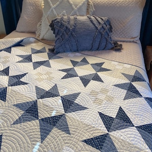 May include: A white and blue quilt with a star pattern. The quilt is on a bed with pillows in shades of beige and blue.