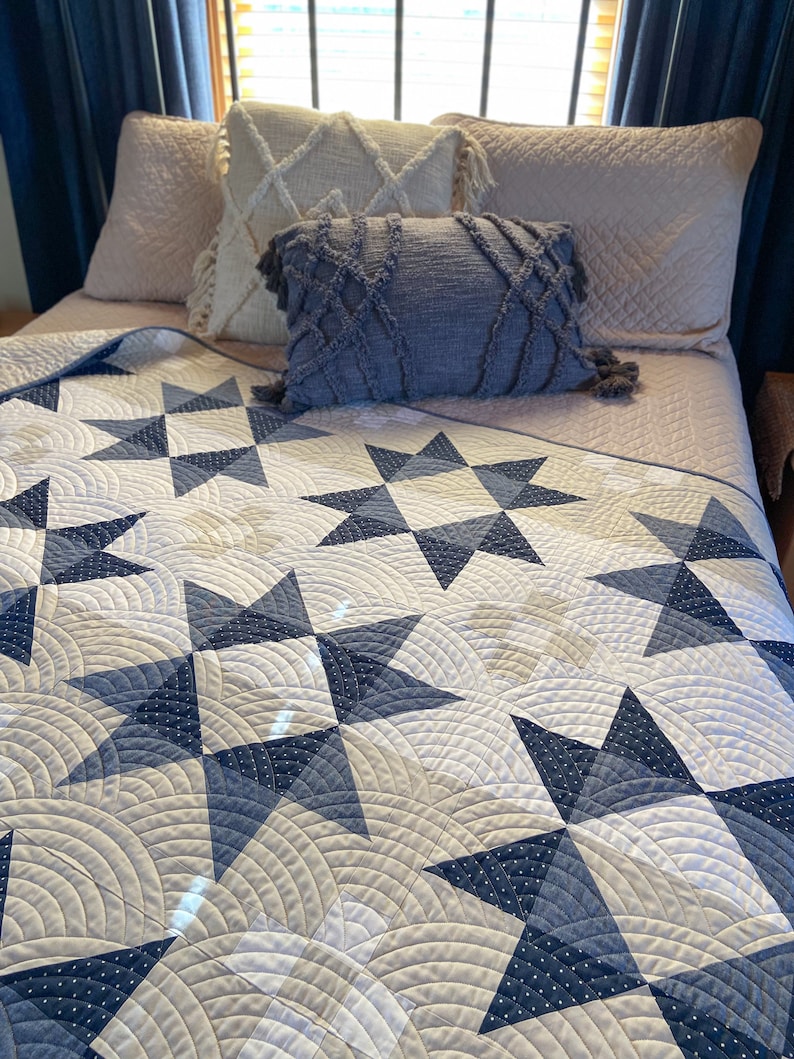 May include: A white and blue quilt with a star pattern. The quilt is on a bed with pillows in shades of beige and blue.