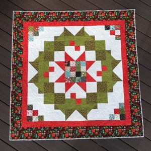 Pode incluir: Um edredom feito à mão com um design de estrela. O edredom apresenta uma estrela central em vermelho e verde, rodeada por blocos brancos e verdes. Uma borda vermelha com padrões florais emoldura o edredom. O edredom tem aproximadamente 152 cm quadrados.