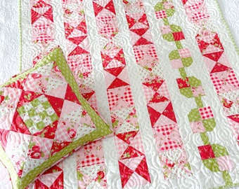 Puede incluir: Una colcha de retazos rosa y verde con un patrón floral. La colcha está hecha con cuadrados y triángulos y tiene un fondo blanco. También se incluye una almohada a juego.