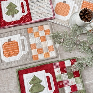Könnte beinhalten: Eine Auswahl handgefertigter, gesteppter Untersetzer mit festlichen Motiven. Die Untersetzer zeigen einen Weihnachtsbaum, einen Kürbis und Patchwork-Muster. Sie sind mit roten, grünen und neutralen Stoffen eingefasst. Auf einem Untersetzer steht der Text "MERRY CHRISTMAS".