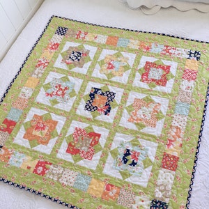 Può includere: Una trapunta patchwork verde e bianca con un motivo floreale. La trapunta è composta da quadrati e rettangoli di tessuti diversi. La trapunta è bordata con un bordo blu scuro.