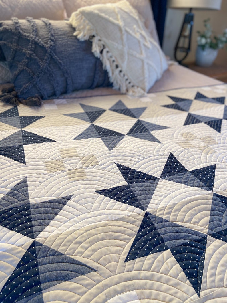 May include: A white and blue quilt with a star pattern. The quilt is made with a white fabric with a subtle texture and a blue fabric with white polka dots. The quilt is folded in half and the edges are visible.