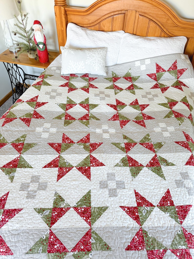 May include: A white, red, and green quilt with a star pattern. The quilt is on a bed with white pillows.