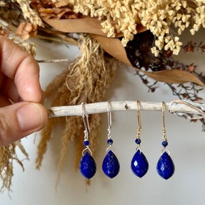 May include: Three pairs of dangle earrings with teardrop-shaped lapis lazuli stones. The earrings are silver and gold toned and feature a small bead at the top of the dangle.