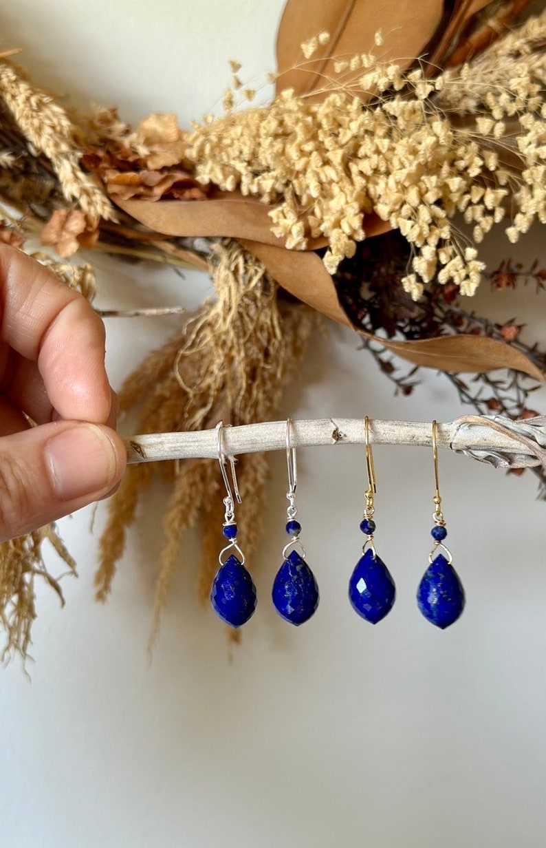 May include: Three pairs of dangle earrings with teardrop-shaped lapis lazuli stones. The earrings are silver and gold toned and feature a small bead at the top of the dangle.