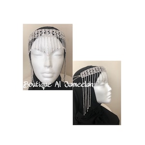 May include: A silver rhinestone headband with a fringe of rhinestones. The headband is worn on a mannequin with a black hijab.