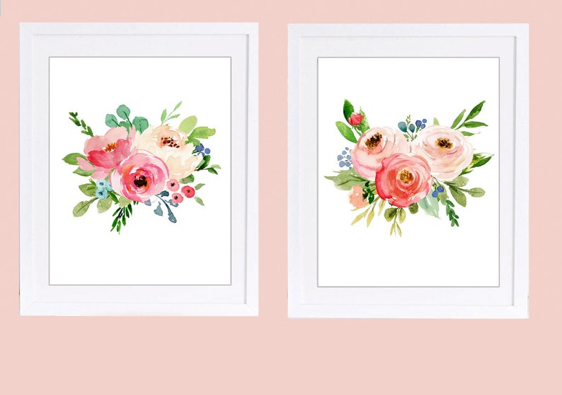 May include: Two framed watercolour floral prints. Each print features a bouquet of pink, peach, and white flowers with green leaves and blue accents. The flowers are arranged in a loose, artistic style, set against a white background.
